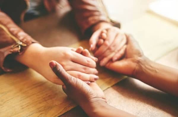 Scene of an African American woman and Caucasian woman holding hands in prayer.