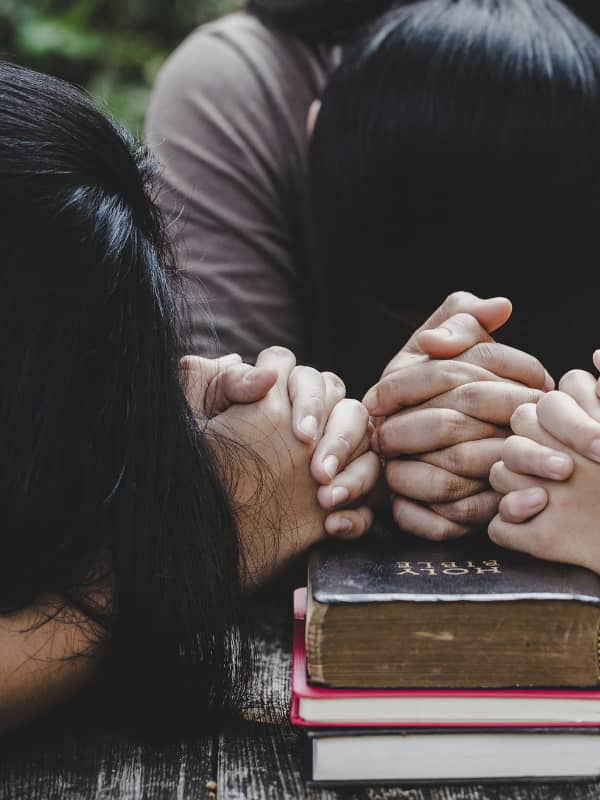 Three women with their heads bowed over the bible and hands in prayer.