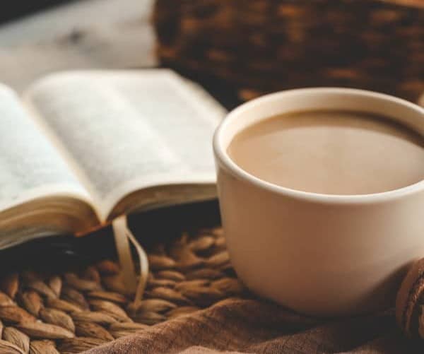 An open bible and mug filled with coffee sitting on a brown table.