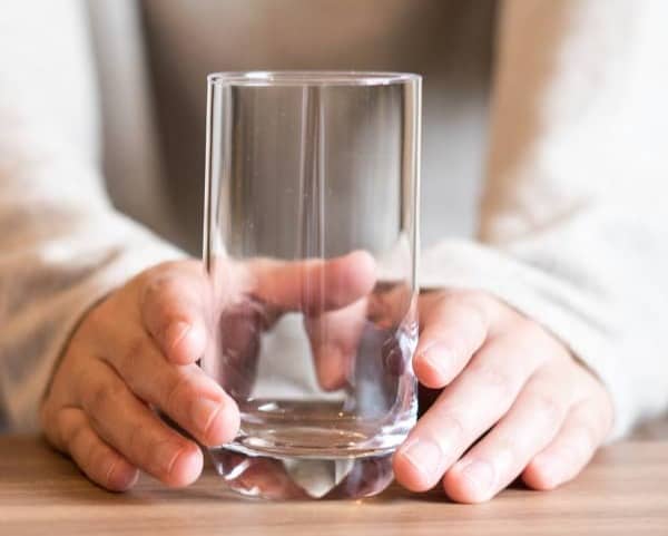 A woman at a table holding an empty glass of water.