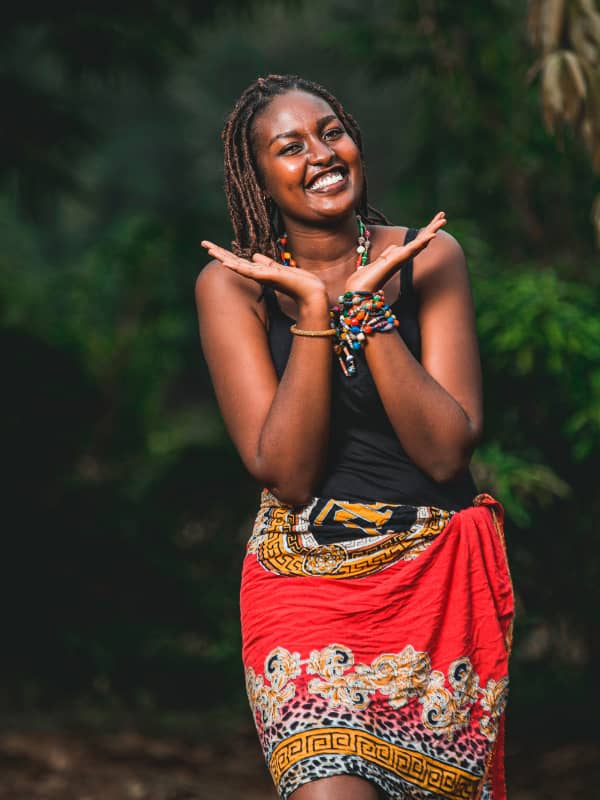 Outside scene with woman wearing an African them wrap skirt and smiling with her hands up.