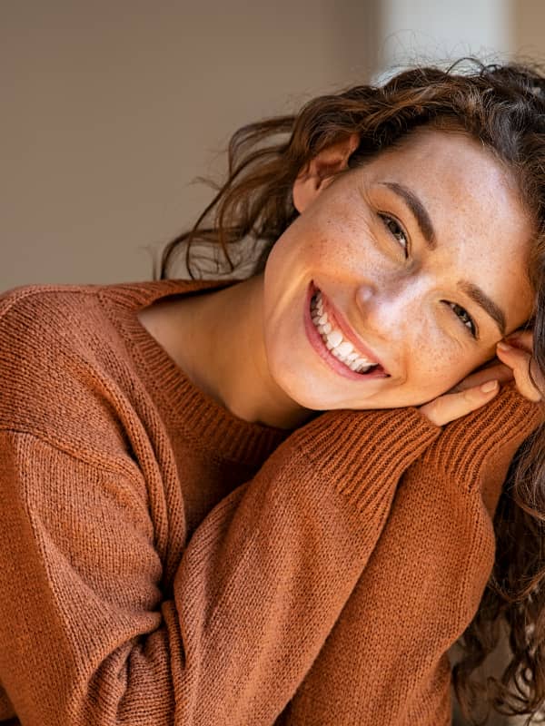 Caucasian woman leaning onto her hands looking into the camera smiling.