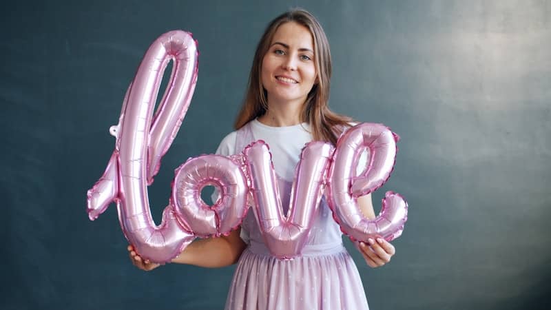 Woman holding pink balloons spelling out the word love.