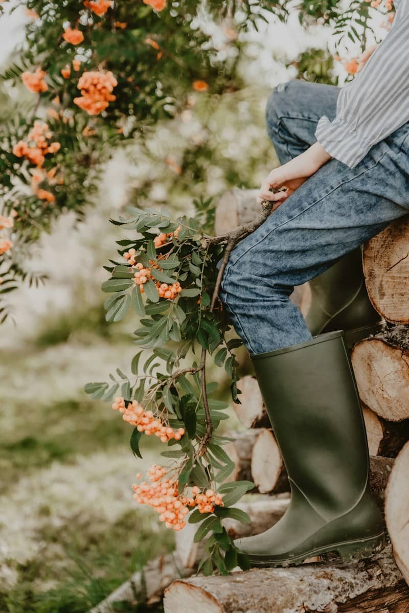A person in blue jeans and green rubber boots sitting on stacked logs