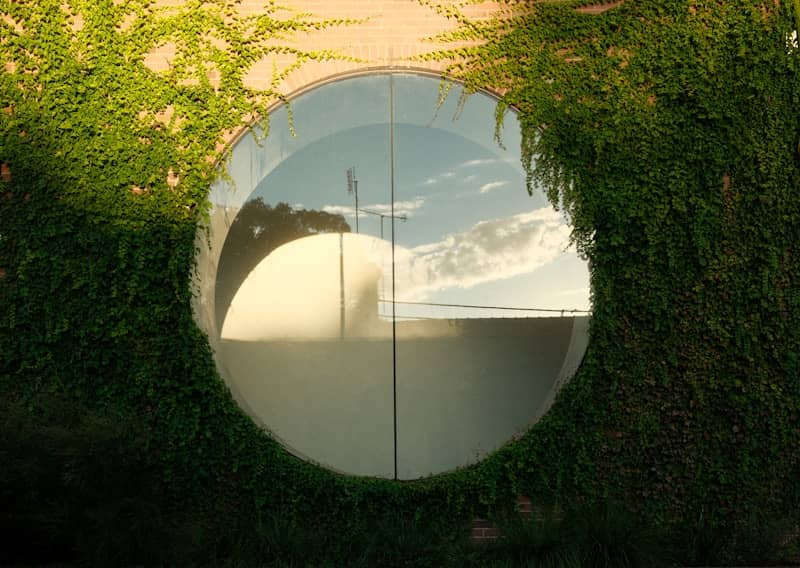 Circular window reflecting sky and trees on brick wall
