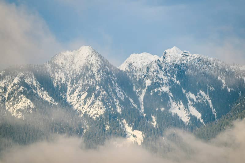 Snow-covered mountains emerge from swirling clouds.