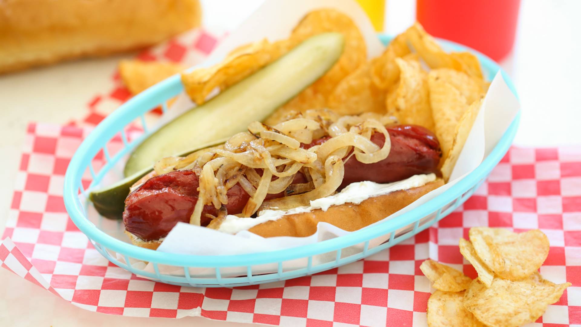 a grilled hot dog in a basket with a pickle and chips