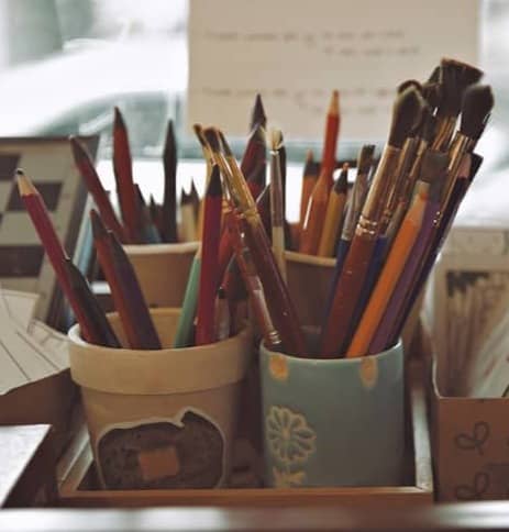 Art supplies in containers with pencils and brushes.