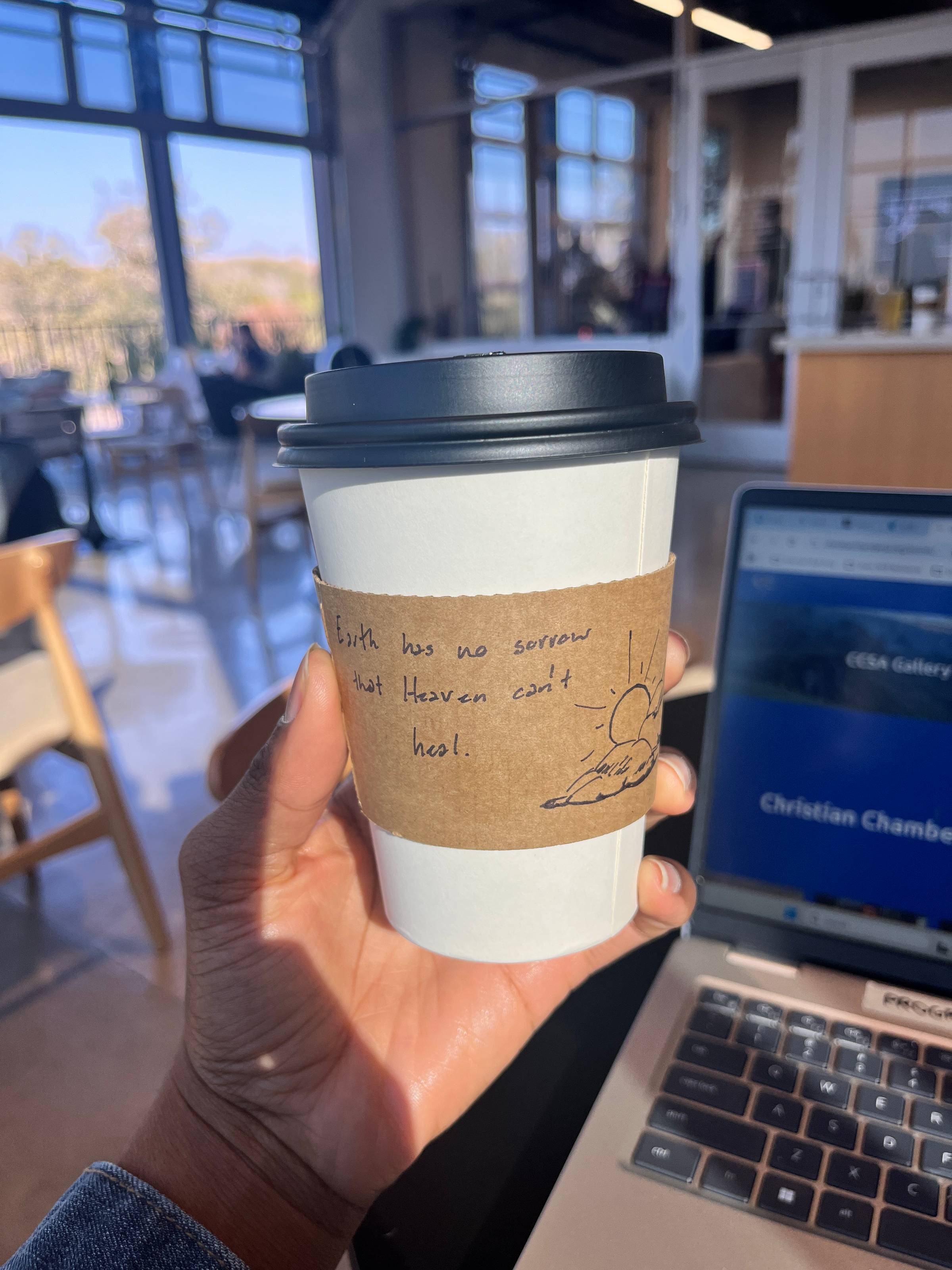 A photo of a to-go coffee cup with the words "Earth has no sorrow that Heaven can't heal," and a drawing of a sun coming out of the clouds.