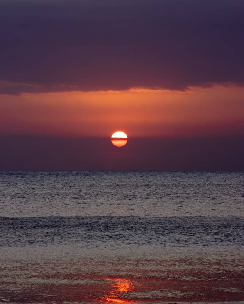 The sun is setting over the ocean on a cloudy day