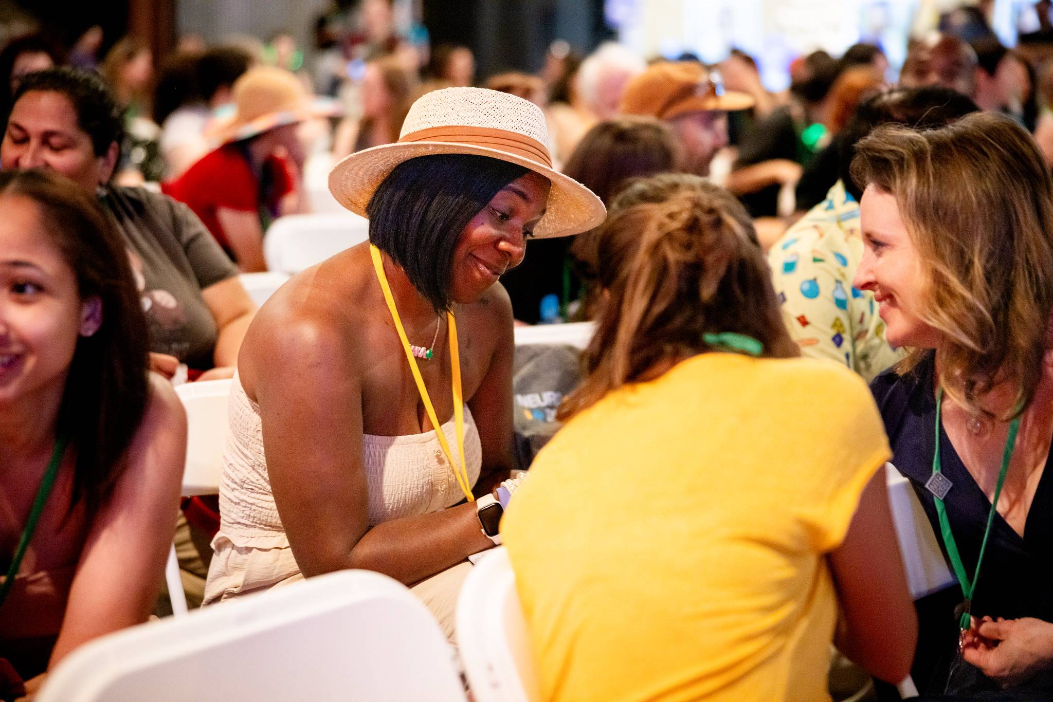 Two NeuroDiversion attendees leaning in to talk at a table, surrounded by a full room