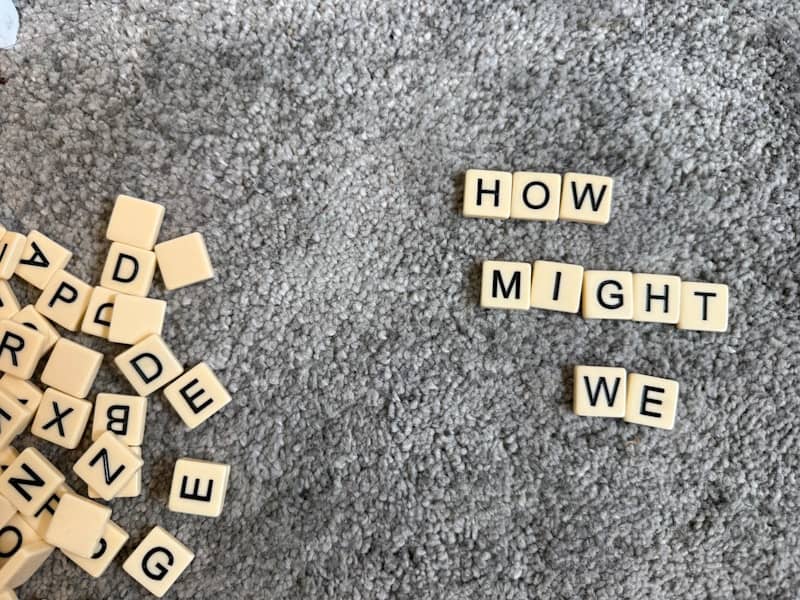 Scrabble tiles spell out "how might we" on carpet.