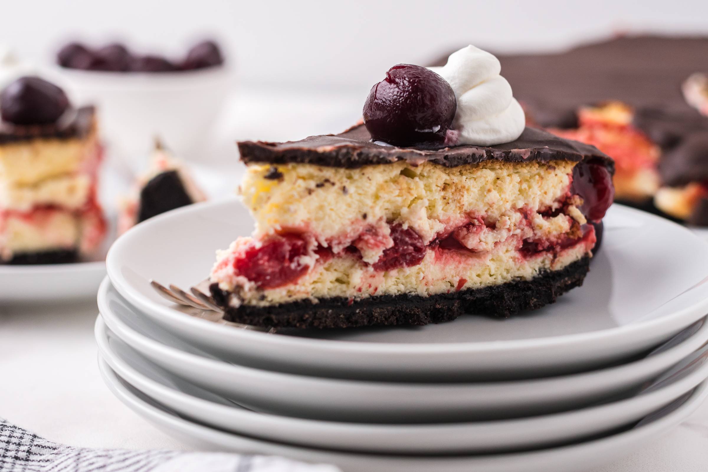 a slice of chocolate cherry cheesecake on a stack of white plates