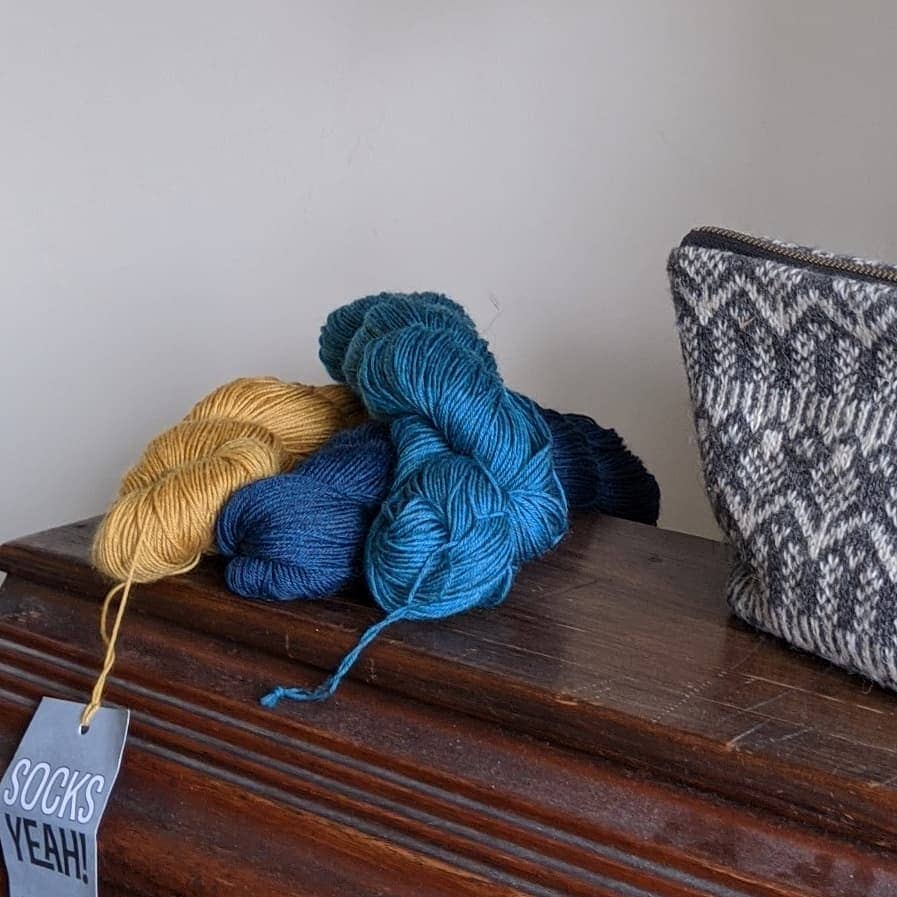 three skeins of yarn sat on a wooden box with a grey wool project bag