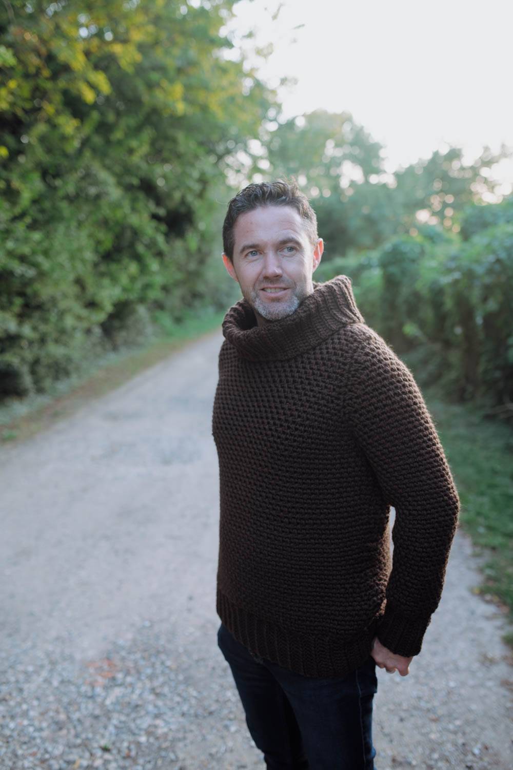 kenny wears brown jumper facing camera against a leafy background