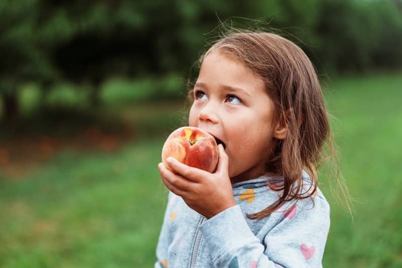 A young girl eating a fresh peach outdoors.