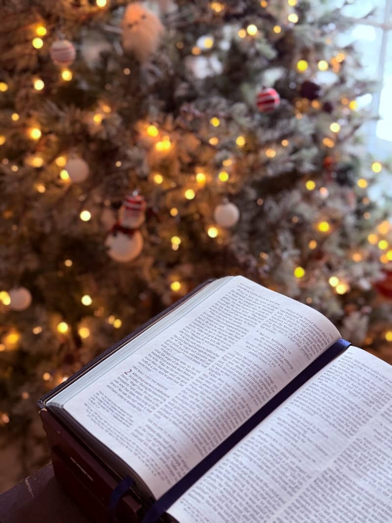 Open bible in front of a decorated christmas tree.