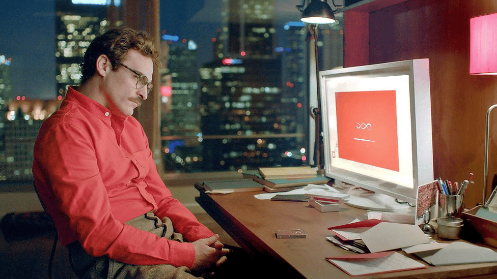 A still from the movie 'Her', showing Theodore Twombly at a desk in front of his computer