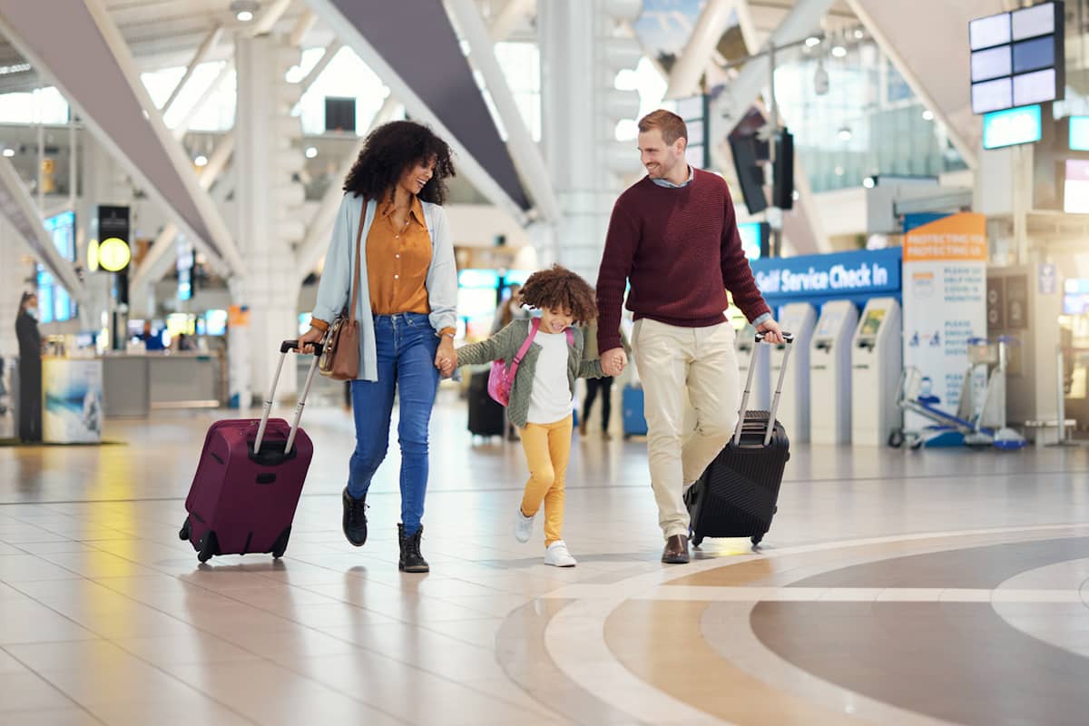 Family with a child walking through an airport terminal with rolling suitcases before a flight.
