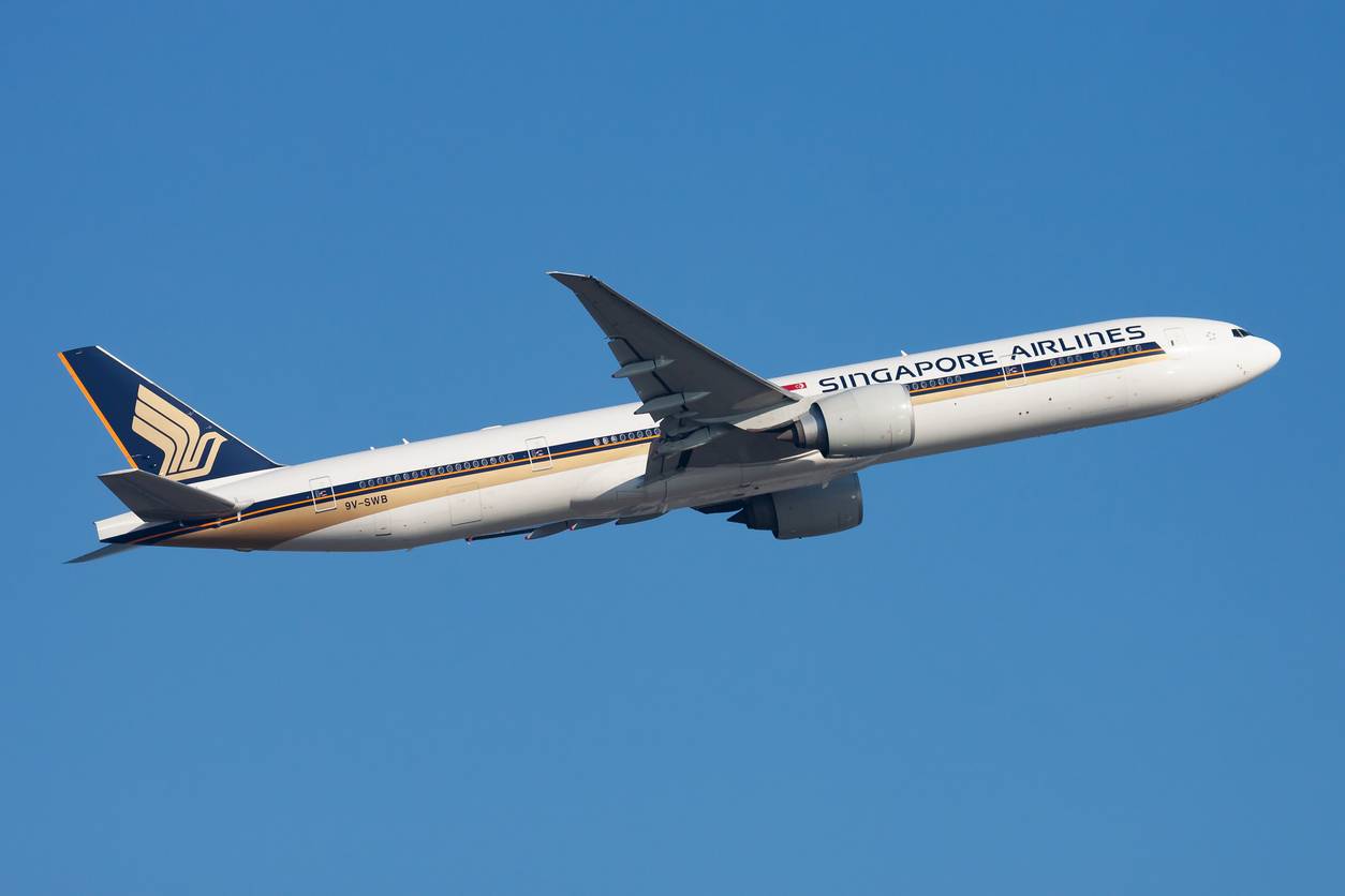 A Singapore Airlines Boeing 777-300ER plane flying in the blue sky.