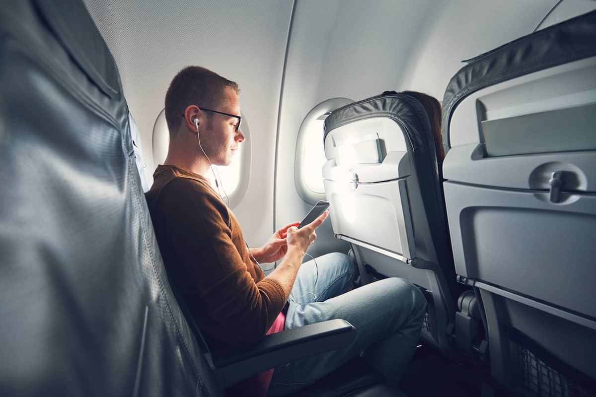 Traveler with earbuds using his phone in an airplane window seat