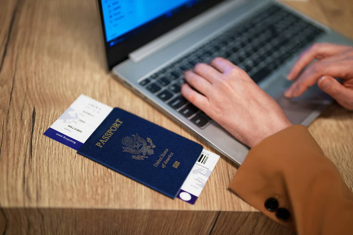 Passport resting on a desk while a traveler types on a laptop