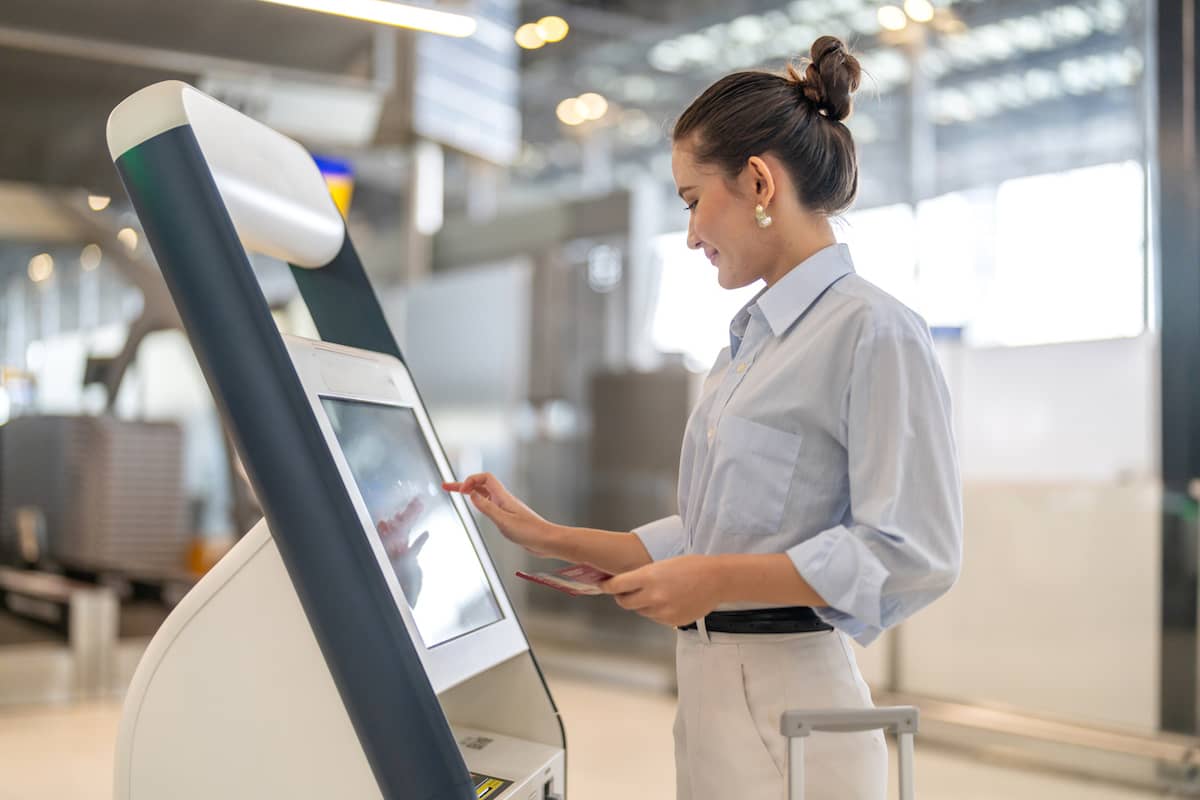 Traveler taps an airport check-in kiosk screen before dropping off her checked bag