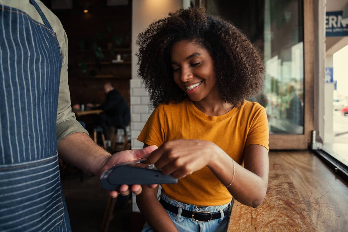 Smiling woman paying at a café card terminal held by a server
