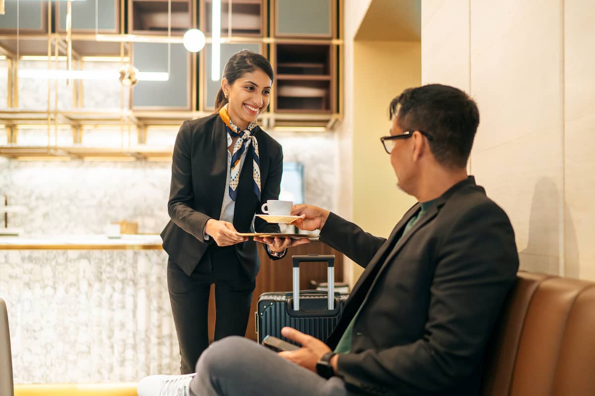 Lounge attendant greets a seated traveler in an airport lounge
