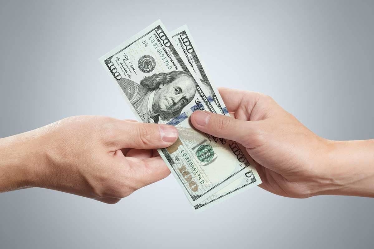 A pair of hands holding two hundred dollar bills