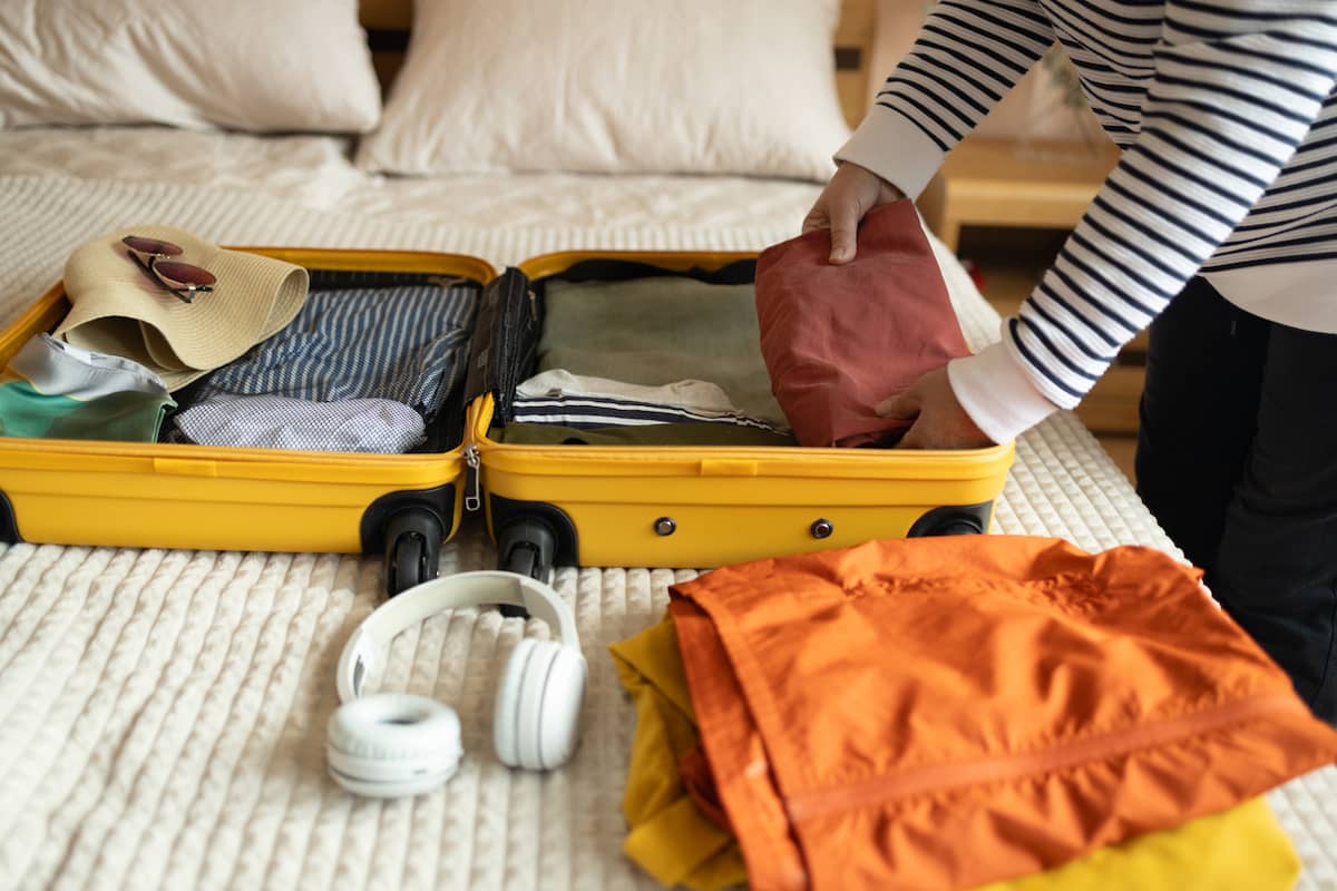 Traveler packing folded clothes into an open yellow suitcase