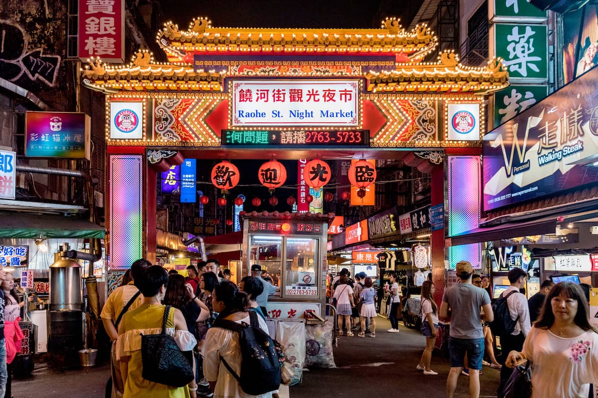 Crowds under the lit-up gate of Raohe Night Market in Taipei