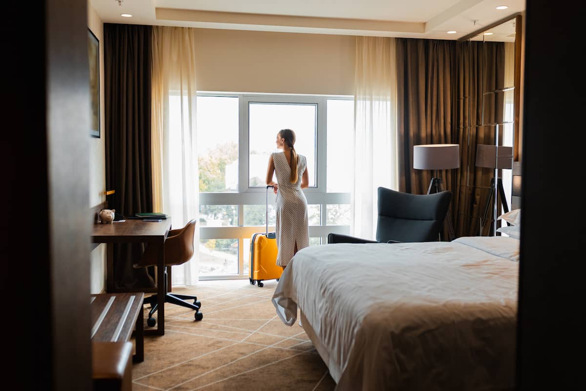 Woman with a yellow carry-on looking out a hotel room window