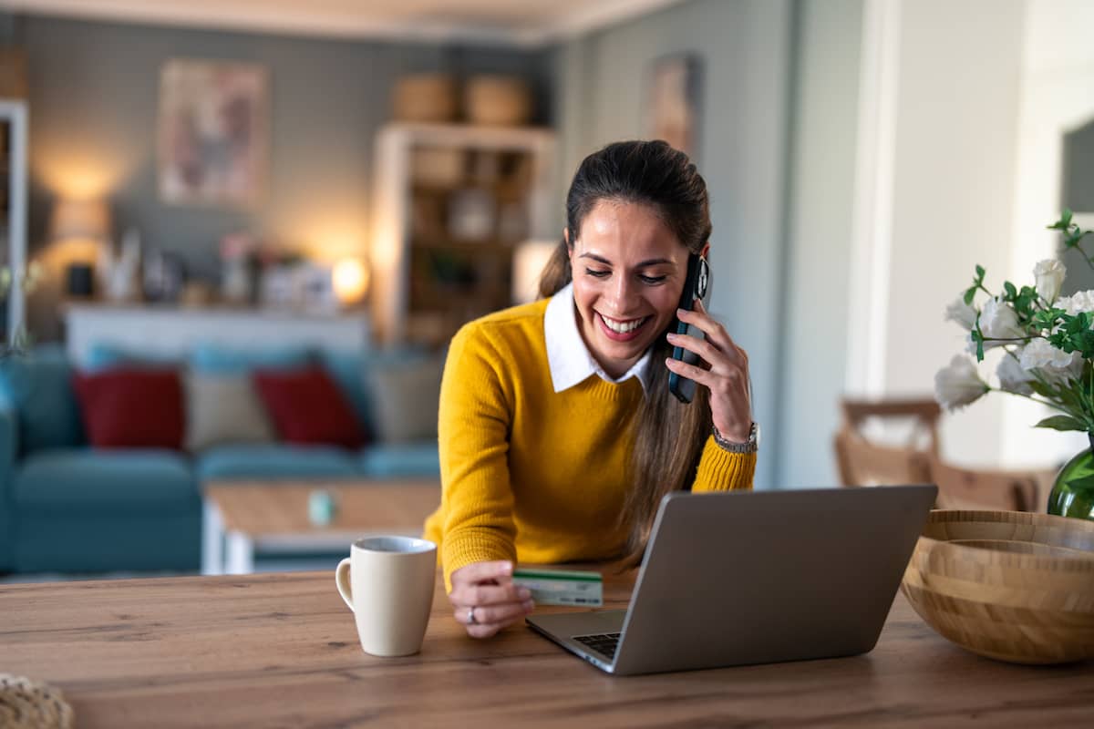Smiling woman on a phone call holding a credit card at her laptop