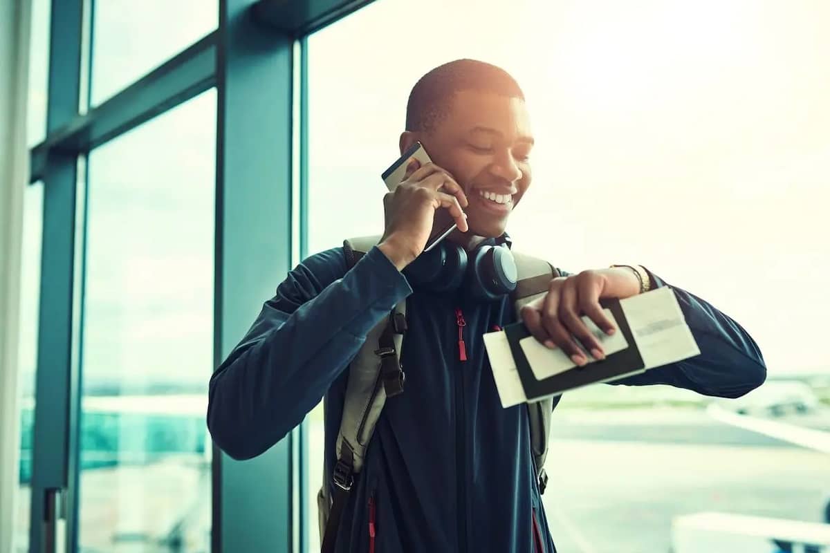 Man at airport holding boarding pass and passport looking at his watch while talking on the phone.
