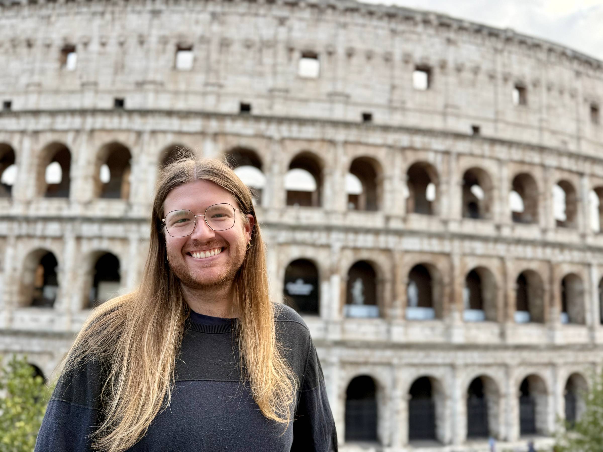 Headshot of the author Harrison Pierce smiling in front of the Colosseum in Rome.