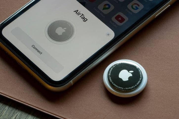 An Apple iPhone sits on a table next to an Apple AirTag