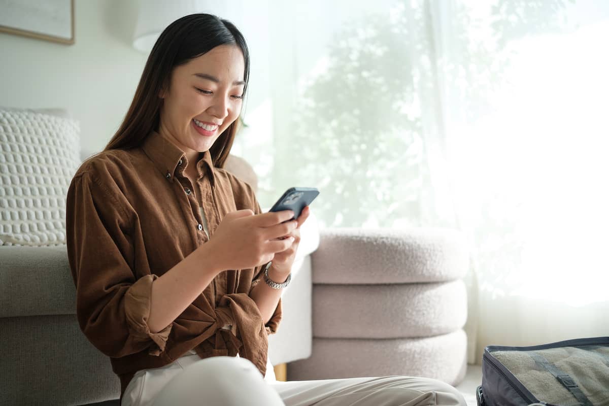 Smiling woman checks trip details on her phone at home with a packing cube beside her