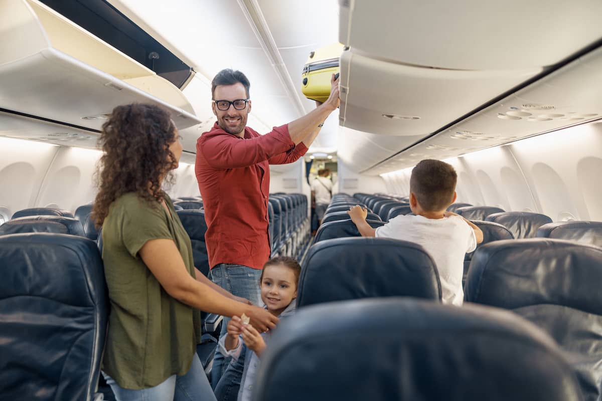 Parents and two young children boarding a plane together, finding their seats in the same row.