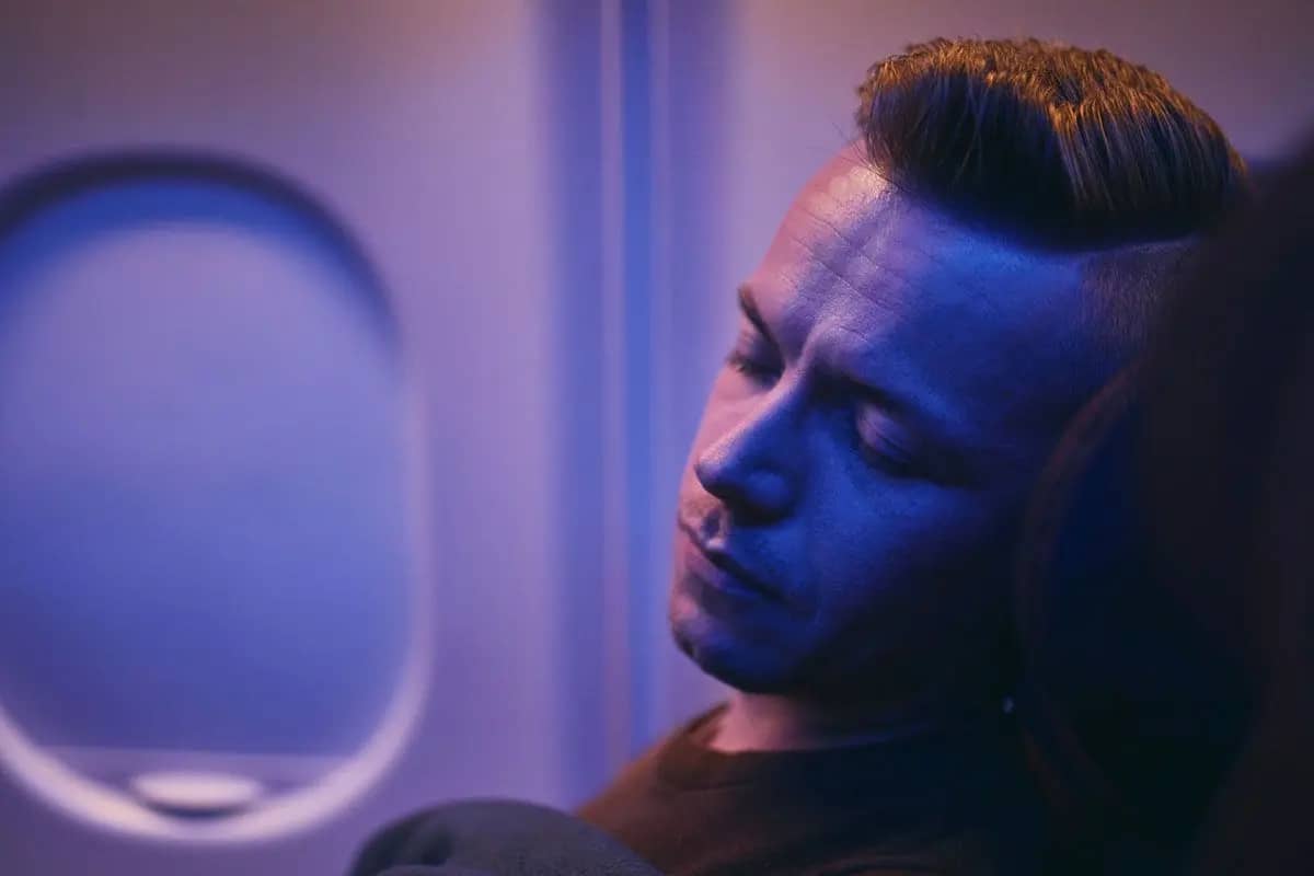 A man sleeping on a plane with a blue light on his face