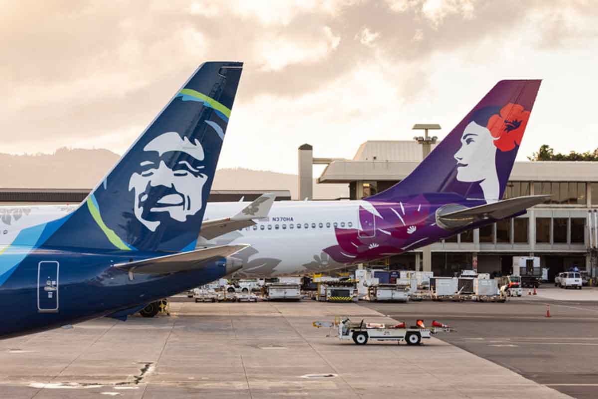 A Hawaiian Airlines plane and an Alaska Air plane sitting on the ground next to each other.