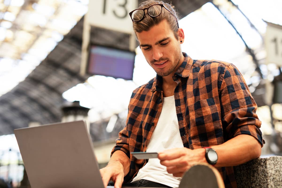 Man holding a credit card while using a laptop at a train station