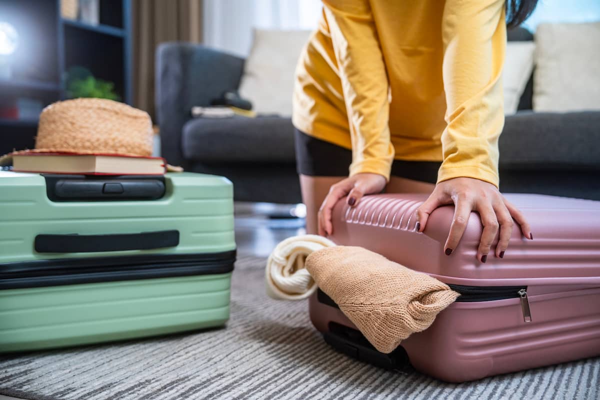 Traveler pressing down on an overstuffed suitcase next to another suitcase