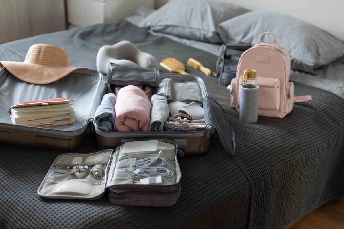 A suitcase surrounded by travel gear sitting on a bed, waiting to be packed.