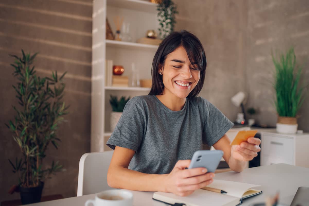 Smiling woman at a desk holding a phone and a credit card