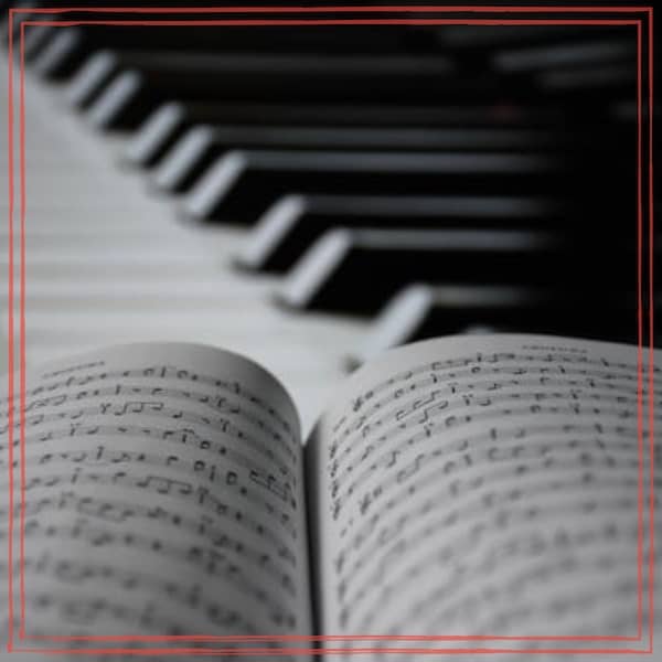 An open music book of sheet music in the foreground, with piano keys receding into the background at an angle.