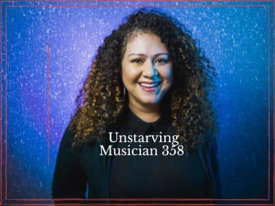Janette Berrios smiling, with long curly hair, wearing a black collared top against a blue and purple backdrop.