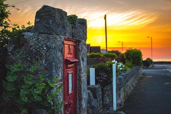 Weathered stone wall with a red metal post box, bathed in warm sunset light