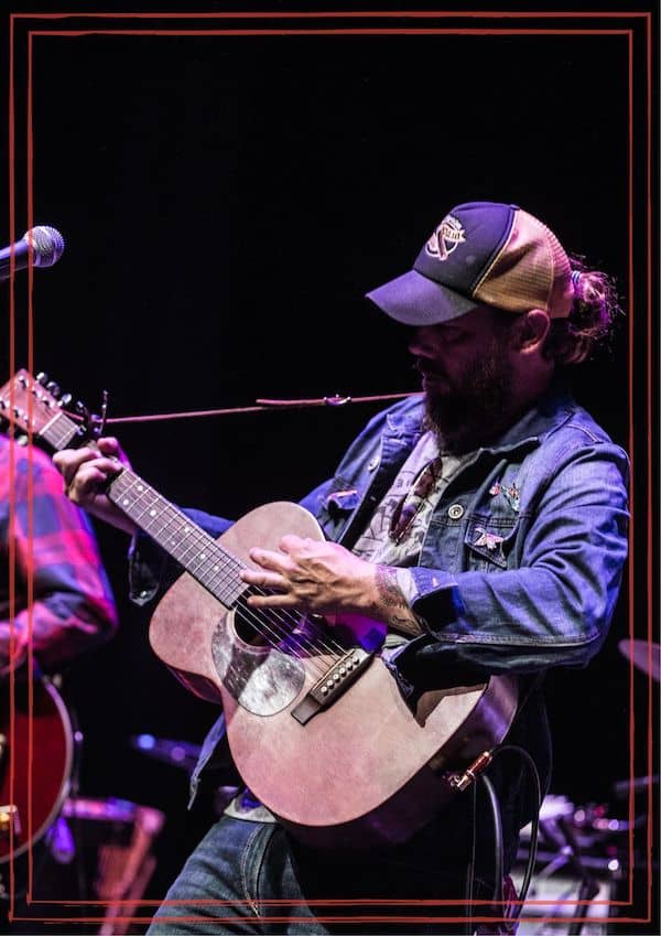 Tony Harrah on stage with acoustic guitar wearing ball cap