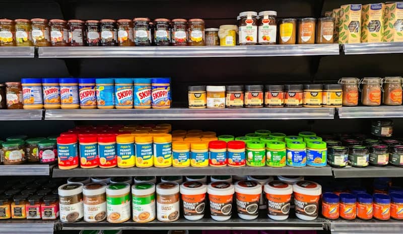 Grocery shelves stocked with various jars and bottles like peanut butter and jams.